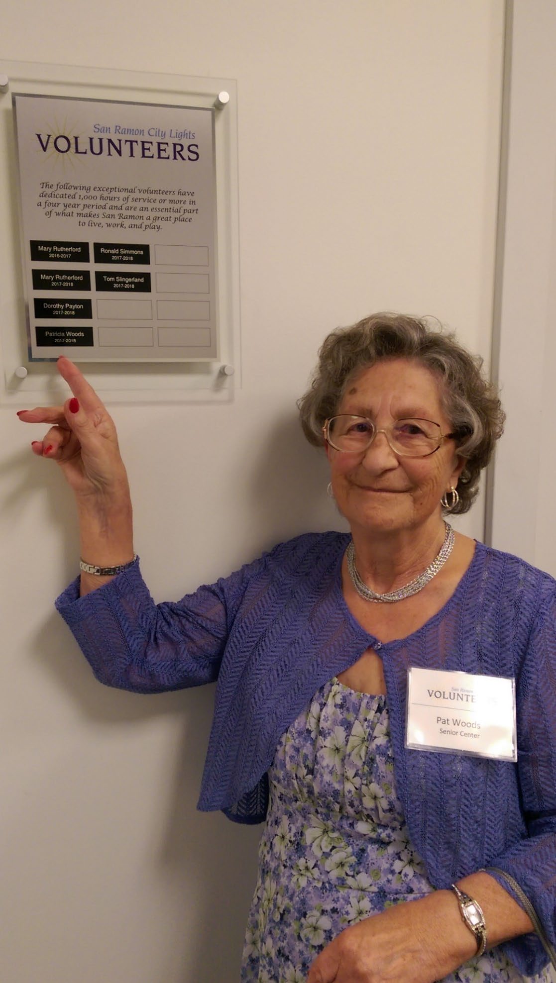 Pat Woods pointing at the volunteer recognition plaque with her name included